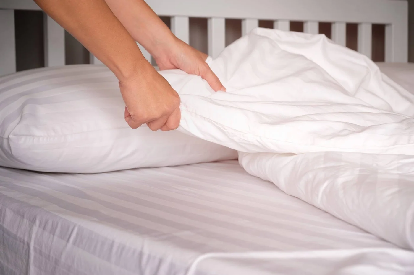 Hands arranging a white comforter on a bed