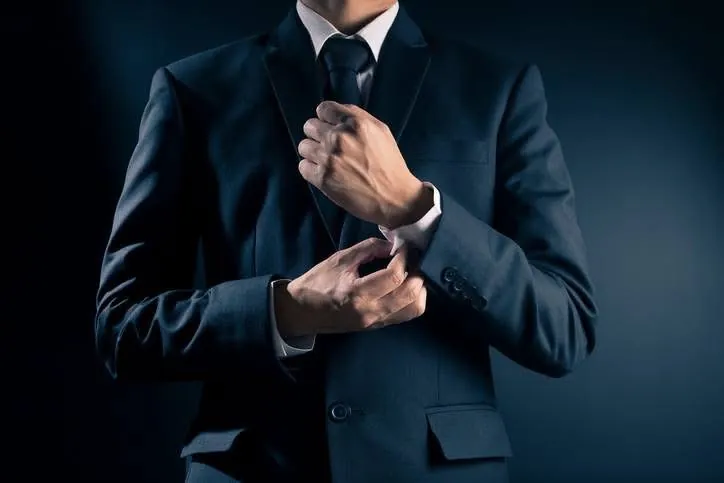 A man in a navy suit adjusting his shirt cuffs