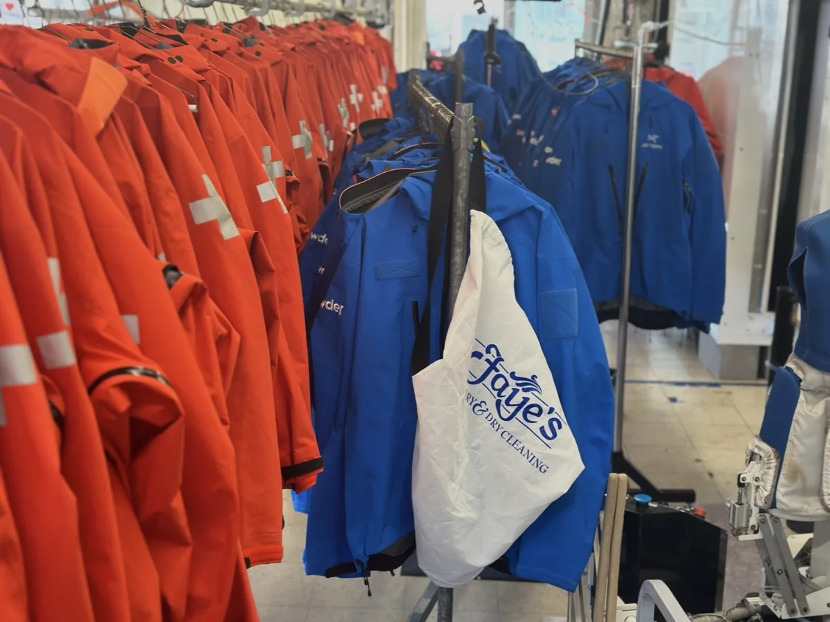 Rows of red and blue garments on racks, with a white Faye's Laundry and Dry Cleaning bag hanging in front