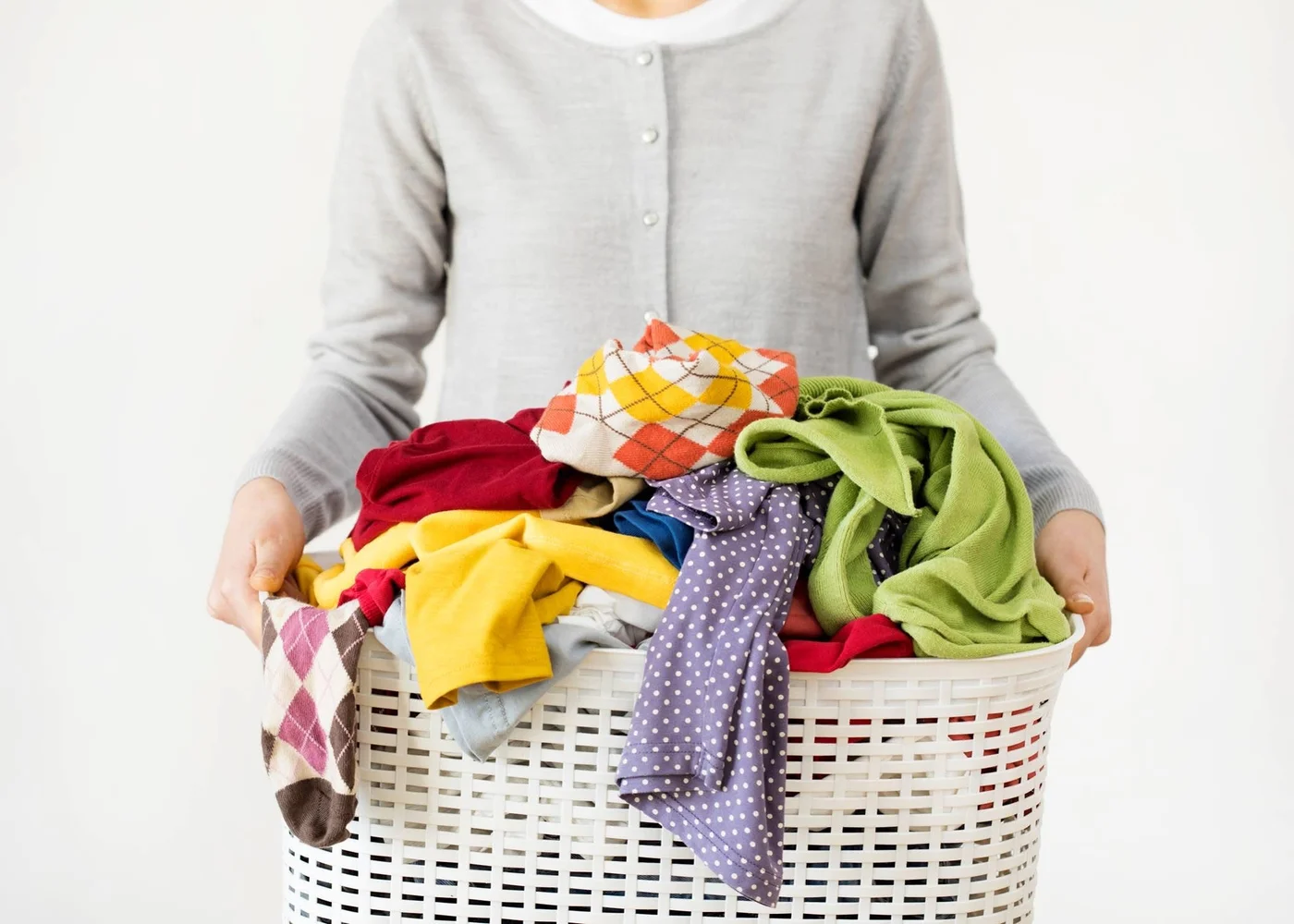 A person holding a white laundry basket filled with colorful everyday clothing